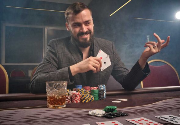 Cheeky brunette man in a classic suit is playing poker sitting a